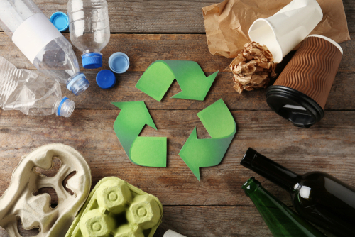 A recycling symbol surrounded by different types of garbage on a wooden surface, emphasizing waste segregation and recycling.