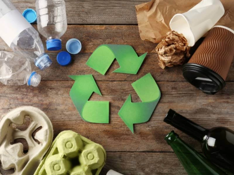 A recycling symbol surrounded by different types of garbage on a wooden surface, emphasizing waste segregation and recycling.