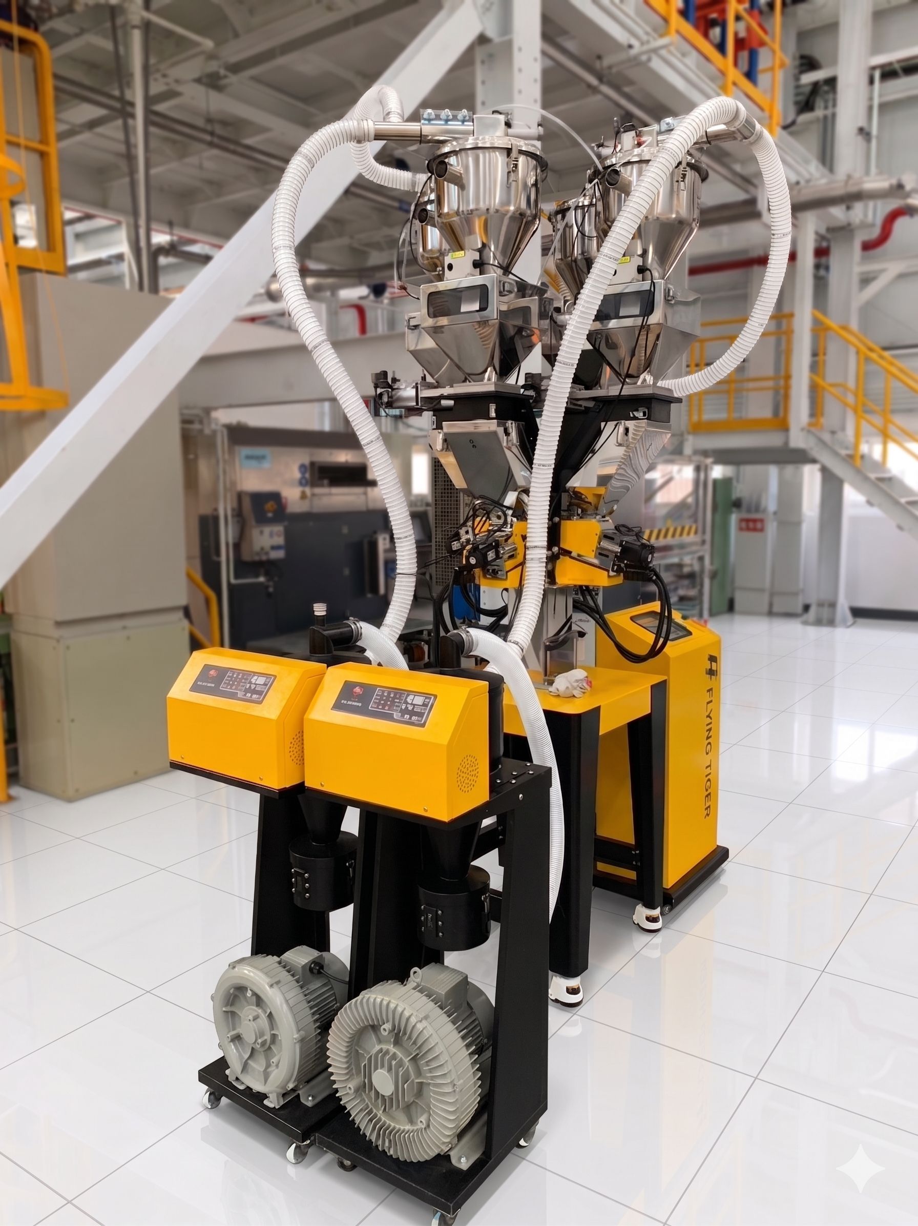 Flying Tiger's Loss-in-weight dosing blender system setup on factory floor. The top features dual central material receivers to receive different kinds of material. In the foreground, two yellow control boxes are vacuum conveying loader.