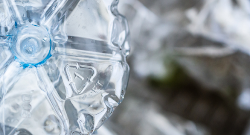 Close-up of a clear, crushed PET water bottle showing detail and texture with the recycling symbol embossed on its surface, against a blurred background.